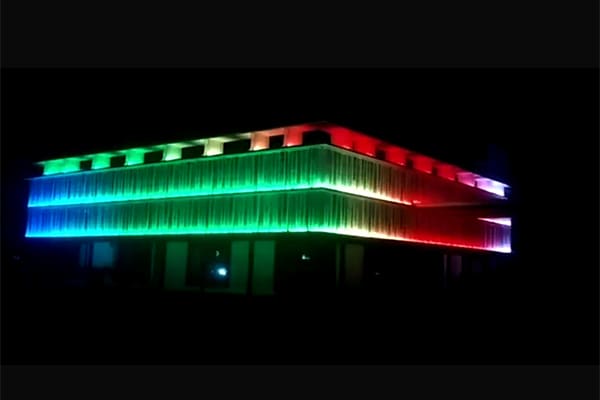 A large building facade illuminated with colorful wall washer lights at night